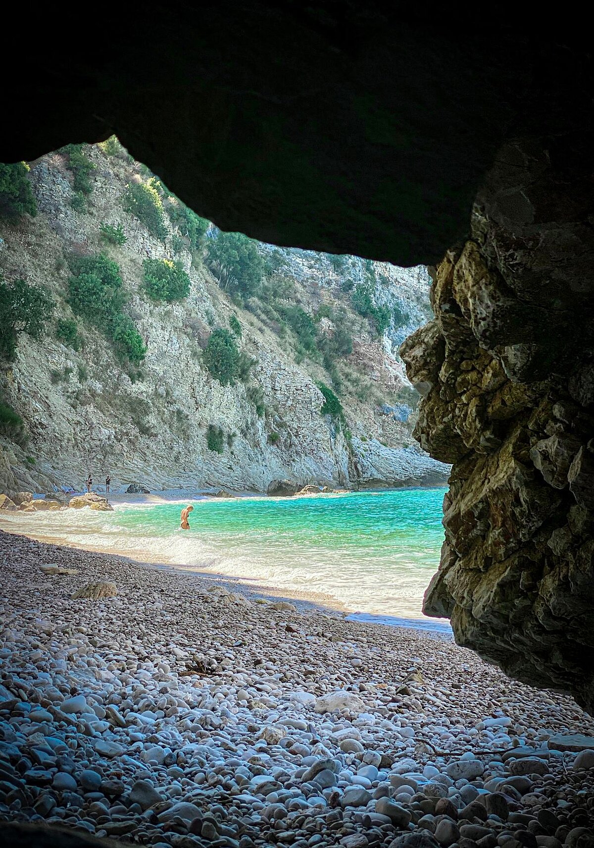 Explore the stunning Albanian coastline from a rocky cave overlooking a turquoise bay.